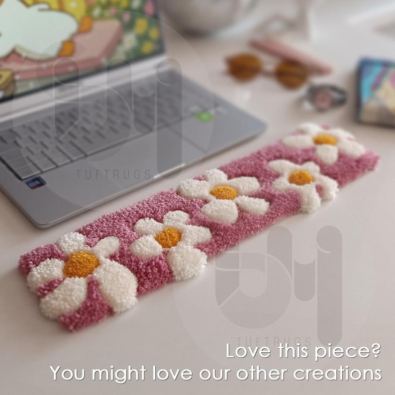 May include: A pink and white tufted rug with a daisy pattern. The rug is made of soft, fluffy yarn and has a unique, handmade look.