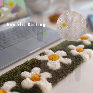 May include: Close-up of a green and white rug with a daisy pattern. The rug has a non-slip backing with small white dots. The text "Tuftrugs" is visible on the rug.
