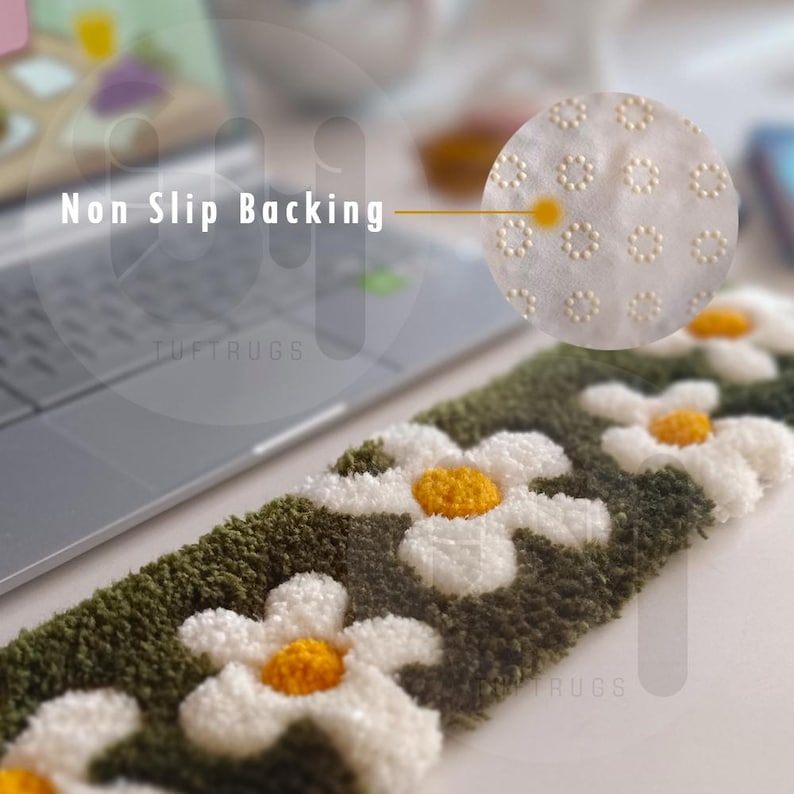 May include: Close-up of a green and white rug with a daisy pattern. The rug has a non-slip backing with small white dots. The text "Tuftrugs" is visible on the rug.