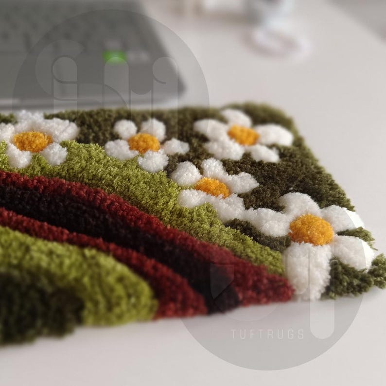 May include: A handmade, tufted rug featuring a daisy design. The rug has a green background with white daisies with yellow centers. Below the daisies are stripes of green and red. The text "TUFTRUGS" is visible.