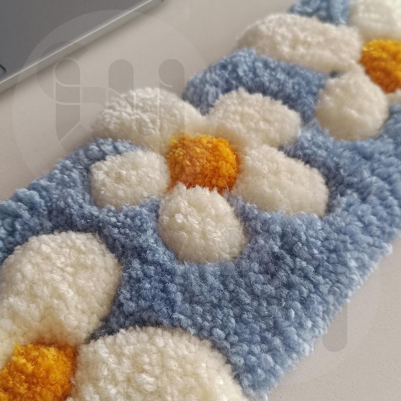 May include: A close-up of a blue, white, and yellow floral design. The design features a daisy pattern with white petals and yellow centers, set against a blue background. The texture appears soft and plush.