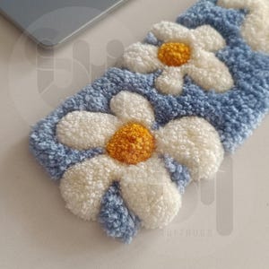 May include: A rectangular, tufted rug with a daisy flower design. The rug features white petals, yellow centers, and a light blue background. The rug is made of a soft, textured material.