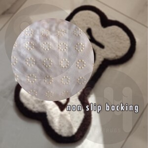 May include: A white bone-shaped rug with a brown outline. The rug has a non-slip backing with small white dots.
