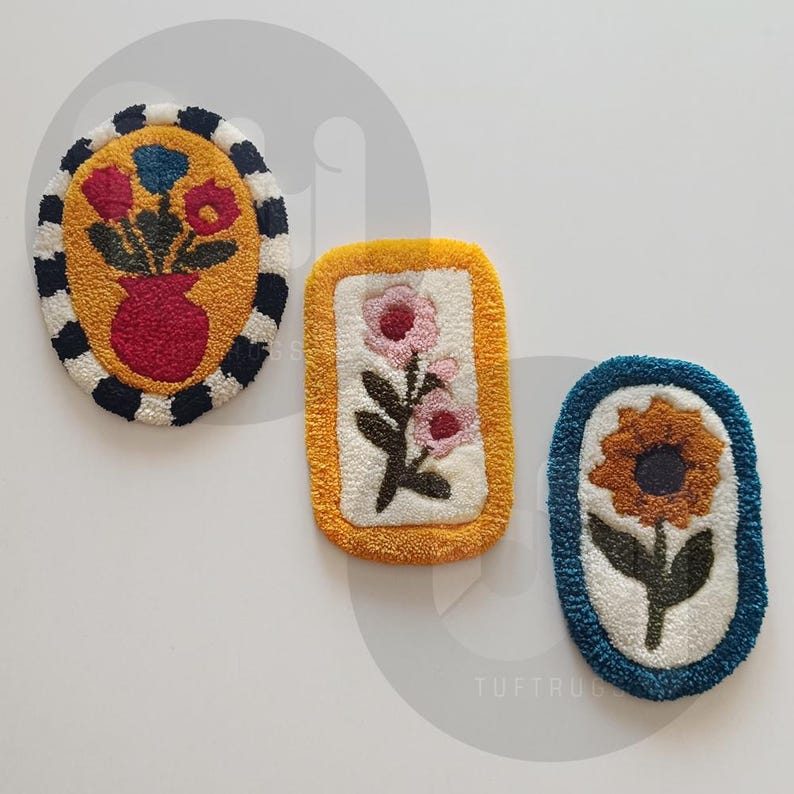May include: Three handmade tufted rugs with floral designs. The first rug is oval shaped with a red vase and blue and red flowers on a white background with black and white trim. The second rug is rectangular with a yellow border and a white background with pink flowers and green leaves. The third rug is oval shaped with a blue border and a white background with a yellow sunflower and green leaves.