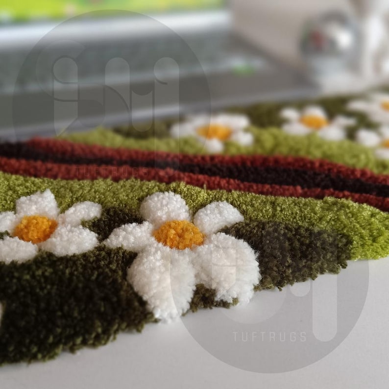 May include: Close-up of a daisy-themed rug with white petals and yellow centers. The rug features green, brown, and red stripes, with the text "TUFTRUGS" visible in the bottom right corner. The rug is likely handmade.