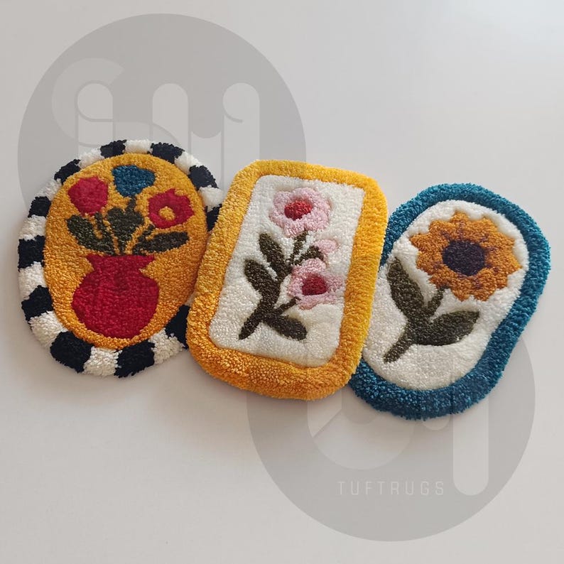May include: Three handmade tufted rugs with floral designs. The rugs are oval and rectangular shaped. One rug features a bouquet of red flowers in a red vase, another rug features a single pink flower with green leaves, and the third rug features a yellow sunflower with green leaves. The rugs are made with a white background and have a black, yellow, or blue border.