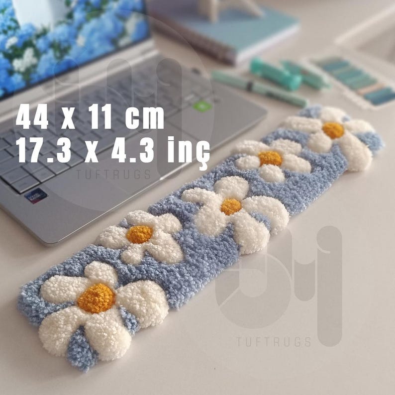 May include: A blue and white daisy-patterned rug, measuring 17.3 x 4.3 inches, rests on a white surface. The rug features a light blue background with white daisy flowers and yellow centers. The text "44 x 11 cm 17.3 x 4.3 in&ccedil;" is visible.
