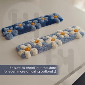 May include: Two rectangular, tufted rugs with daisy patterns. One is light blue with white and yellow daisies, the other is dark blue with white and yellow daisies. The text "TUFTRUGS" is visible. The text "Be sure to check out the store for even more amazing options! :)" is also visible.
