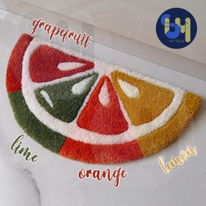 Peut inclure: Un tapis touffeté coloré en forme de tranche d'agrume. Le tapis présente des sections rouges, oranges, jaunes et vertes, avec des accents blancs. Les mots "grapefruit", "lime", "orange" et "lemon" sont écrits sur le tapis.