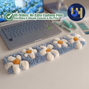 May include: A blue rectangular rug with white daisy flowers and yellow centers. The rug is placed on a white surface near a laptop. The text "US Orders: No Extra Customs Fees Everything Is Already Covered in the Price" is visible.