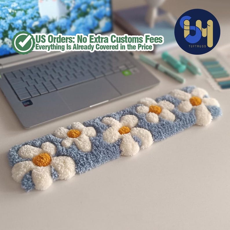 May include: A blue rectangular rug with white daisy flowers and yellow centers. The rug is placed on a white surface near a laptop. The text "US Orders: No Extra Customs Fees Everything Is Already Covered in the Price" is visible.