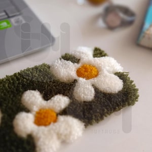 May include: A close-up of a green and white tufted rug with a daisy pattern. The rug is made of soft, fluffy material and has a subtle sheen.