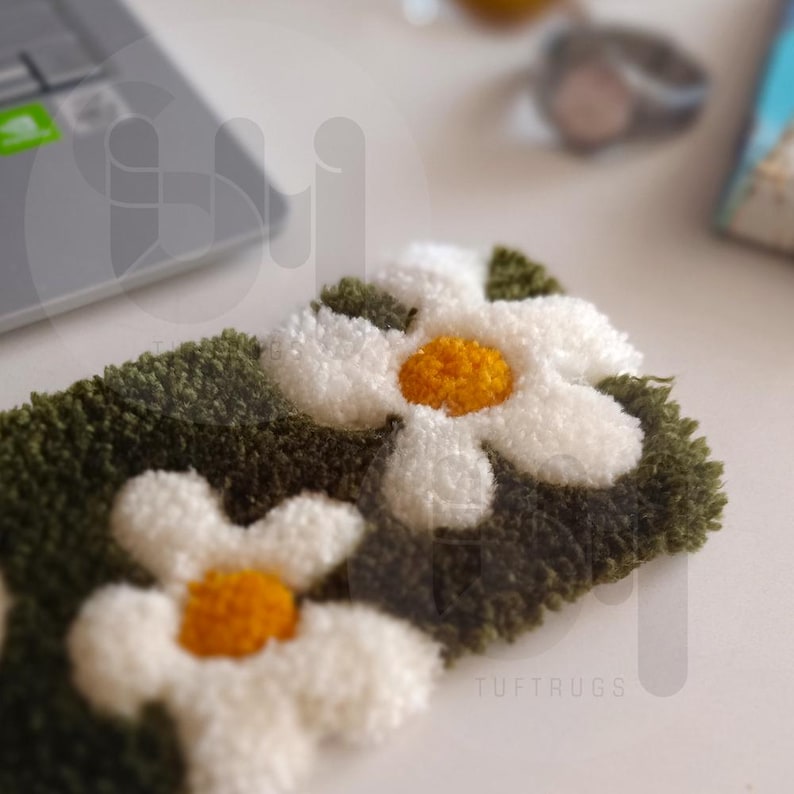 May include: A close-up of a green and white tufted rug with a daisy pattern. The rug is made of soft, fluffy material and has a subtle sheen.