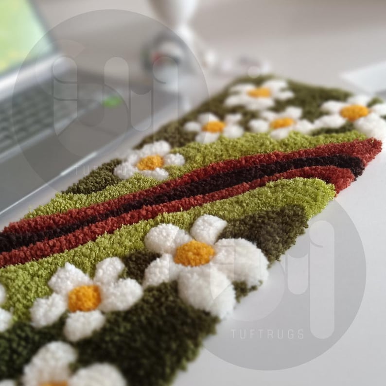 May include: A rectangular, textured rug with a daisy pattern. The rug features white daisies with yellow centers, set against a green and brown background. The text "TUFTRUGS" is visible on the bottom right.
