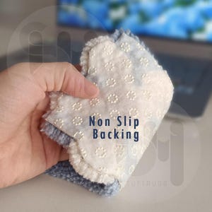 May include: A close-up of a blue and white rug pad with the text "Non Slip Backing". The pad has a textured, dotted white surface and a blue, fluffy border. The pad is being held up.