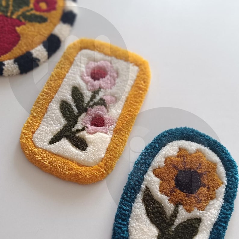 May include: Three embroidered patches with floral designs. The first patch is yellow with a black and white stripe border and features a red flower. The second patch is yellow with a white background and features two pink flowers. The third patch is teal with a white background and features a yellow sunflower.