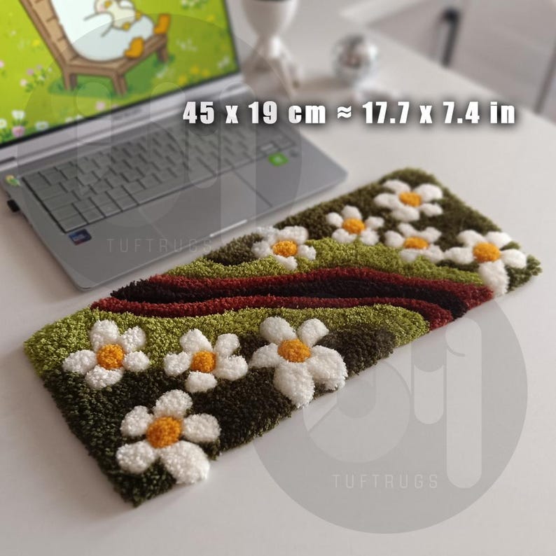 May include: A rectangular, hand-tufted rug with a floral design. The rug features white daisies with yellow centers on a green and brown background. The rug measures approximately 17.7 x 7.4 inches. The brand name "TUFTRUGS" is visible.