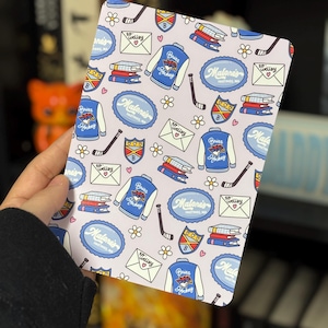 May include: A notebook with a light purple background featuring a pattern of hockey-themed illustrations. The design includes hockey jackets, hockey sticks, books, shields, and envelopes with the text "Briar Hockey" and "Malone's Hastings, MA".