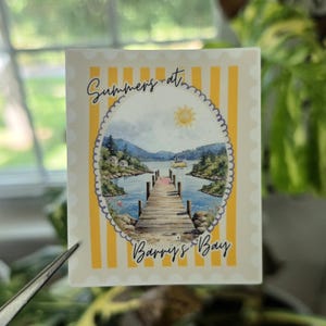 May include: A rectangular sticker with a yellow and white vertical striped border. The center features an oval illustration of a wooden dock extending into a lake surrounded by hills and trees, with the text Summers at Barry's Bay printed in black.