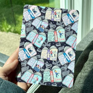 May include: A rectangular, patterned item featuring a repeating design of open books, ice skates, and couples. The books have titles like "The Score", "The Goal", and "The Deal". The background is a dark blue with white stars.