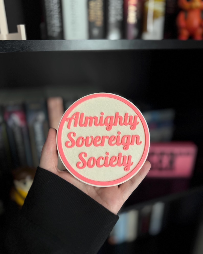 May include: A white round coaster with a pink border and the text "Almighty Sovereign Society" in pink lettering.
