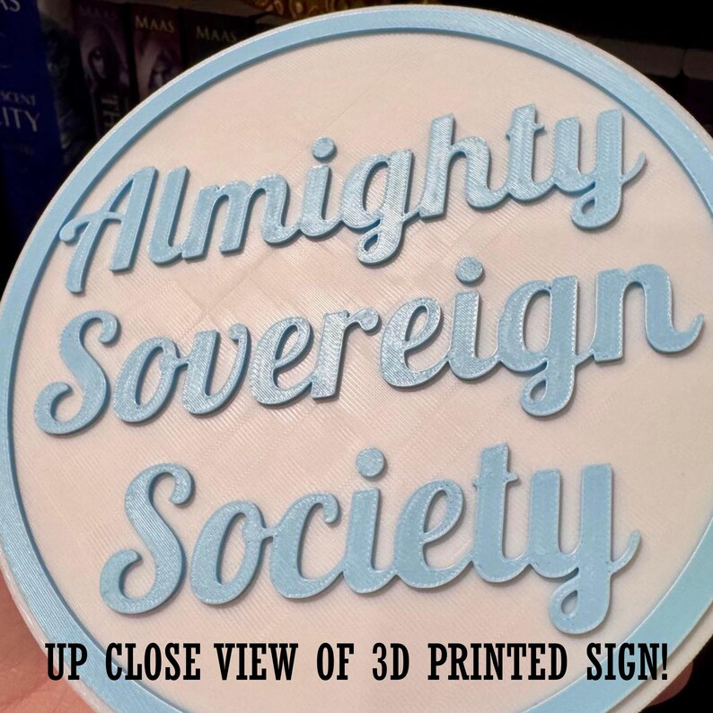 May include: A round, 3D-printed sign with the words "Almighty Sovereign Society" in light blue script. The sign has a light blue border and a white background. The text "UP CLOSE VIEW OF 3D PRINTED SIGN!" is at the bottom.