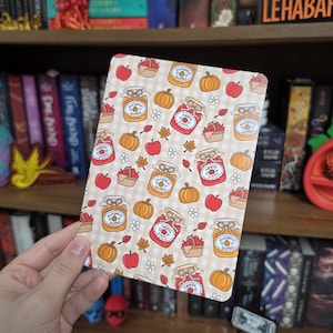 May include: A rectangular print featuring a repeating pattern of orange pumpkins, red apples, small picnic baskets filled with apples, and glass jars labeled pumpkin butter or apple jam, all set against a light beige and white checkered background.