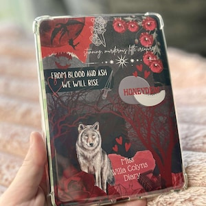 Könnte beinhalten: Eine transparente Schutzhülle für ein Tablet mit einem Design mit einem Wolf, roten Blumen und Text. Der Text enthält "FROM BLOOD AND ASH WE WILL RISE" und "stunning, murderous little creature". Der Hintergrund ist dunkelrot und schwarz.