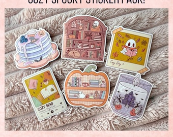 May include: A set of six stickers with a cosy and spooky theme. Designs include pancakes, bookshelves, a ghost reading, a pumpkin-shaped bookshelf, a candle with a haunted house, and a polaroid with a ghost. The text "COZY SPOOKY STICKER PACK!" is at the top.