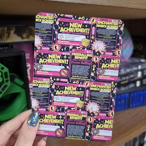 May include: A rectangular card featuring a dark background with repeating graphic panels. The text includes "NEW ACHIEVEMENT!", "ENCHANTED BIGBOI BOXERS", and "FREEBALLING BENEFFIT". The design incorporates icons of boxers, treasure chests, and skulls in vibrant pink, yellow, and white colors.