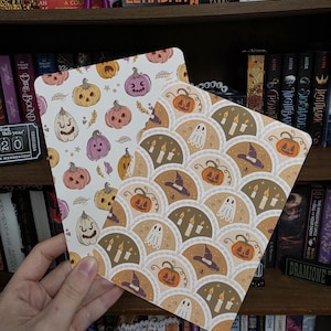 May include: Two rectangular cards featuring Halloween-themed illustrations. One card displays a white background with scattered orange and purple jack-o'-lanterns. The second card features a scalloped pattern containing orange pumpkins, white ghosts, purple witch hats, and lit candles.
