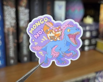 Könnte beinhalten: Ein gestanzter Aufkleber mit einem blauen gefiederten Dinosaurier, auf dessen Rücken eine Glückskatzen-Katze mit einer rosa Schutzbrille sitzt. Der Text "MONGO, NO!" steht in Gelb über der Katze. Der Hintergrund ist hellviolett mit gelben Akzenten.