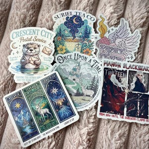 May include: A collection of fantasy-themed stickers featuring illustrations of an otter, a teacup, a castle, a winged object, and tarot card designs. The stickers have various text elements, including "Crescent City Postal Service" and "Once Upon a Time."