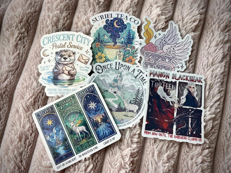 May include: A collection of fantasy-themed stickers featuring illustrations of an otter, a teacup, a castle, a winged object, and tarot card designs. The stickers have various text elements, including "Crescent City Postal Service" and "Once Upon a Time."