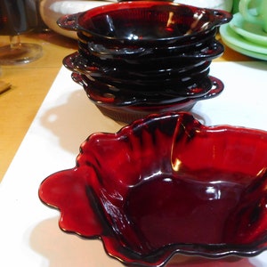 May include: A set of six ruby red glass bowls. The bowls are stacked on top of each other. The bowl on top is a scalloped design.