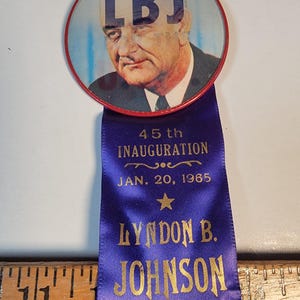 May include: A blue ribbon with gold lettering reads "45th Inauguration Jan. 20, 1965" and "Lyndon B. Johnson Our 36th President". A red button with a picture of Lyndon B. Johnson and the letters "LBJ" is attached to the ribbon.