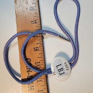 May include: A blue bolo tie with a white button featuring a map of the United States and the text "VOTE L.B.J. '64".