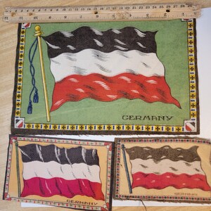 May include: Three vintage fabric patches featuring the German flag. Each patch has a black, white, and red flag with a gold pole and the word "GERMANY" printed below. The patches are framed with a yellow and black border.
