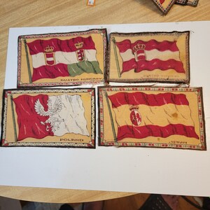 May include: Four vintage fabric patches with flags of Austria-Hungary, Poland, Spain, and Austria-Hungary. The patches are rectangular and have a brown border with a decorative pattern. The flags are printed on the fabric and feature the national colors and emblems.