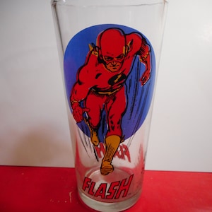May include: A clear glass featuring a graphic of the Flash in a running pose, set against a blue background. The character is depicted in a red suit with yellow boots. The word "FLASH" is printed at the bottom.