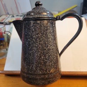 May include: A black and white speckled enamel coffee pot with a black handle and lid. The pot has a classic design and is perfect for brewing coffee.