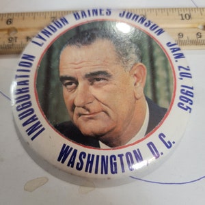May include: A white button with blue and red trim. The button features a portrait of Lyndon B. Johnson and the text "Inauguration Lyndon Baines Johnson Jan. 20, 1965 Washington D.C."