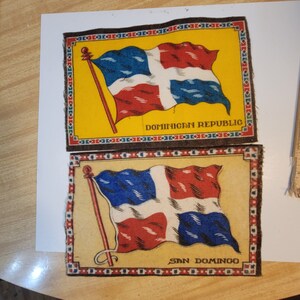 May include: Two vintage fabric patches featuring the Dominican Republic flag. The top patch has a yellow background with the text "DOMINICAN REPUBLIC". The bottom patch has a beige background with the text "SAN DOMINGO".