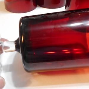 May include: A set of four red glass tumblers with a clear glass base. The tumblers are stacked on top of each other.