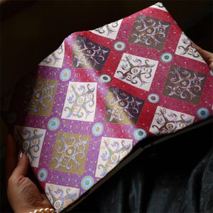 May include: A rectangular clutch bag featuring a repeating diamond pattern in shades of magenta, purple, and cream. Each diamond contains a stylized, symmetrical graphic design with intricate lines and small circular accents in blue and gold.