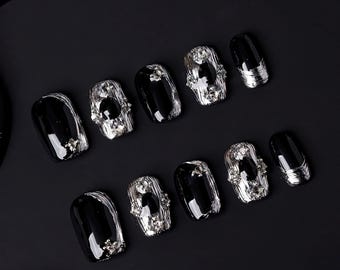 May include: Ten black and silver press-on nails with rhinestones. The nails are arranged in two rows of five.