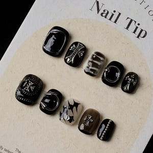 Peut inclure: Un ensemble de dix embouts d'ongles noirs et argentés avec différents motifs, notamment des croix, des clous et des motifs géométriques. Les embouts d'ongles sont présentés sur une carte blanche avec le texte "COLLECTION Nail Tip".