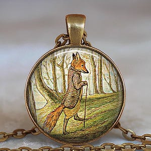 May include: A round pendant necklace with a detailed illustration of a fox in a suit walking with a cane through a forest. The pendant has a gold-colored frame and chain. The fox is orange and brown.