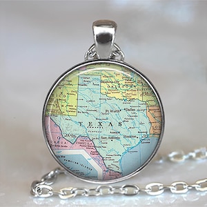 May include: Silver-toned pendant necklace featuring a circular charm with a map of Texas. The map includes cities like Dallas, San Antonio, and Houston. The pendant hangs from a silver chain. The charm has a clear, protective covering.