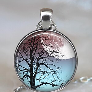 K&ouml;nnte beinhalten: Eine silberne Halskette mit einem runden Glasanh&auml;nger, der eine schwarze Silhouette eines Baumes vor dem Hintergrund eines roten und blauen Mondes zeigt.